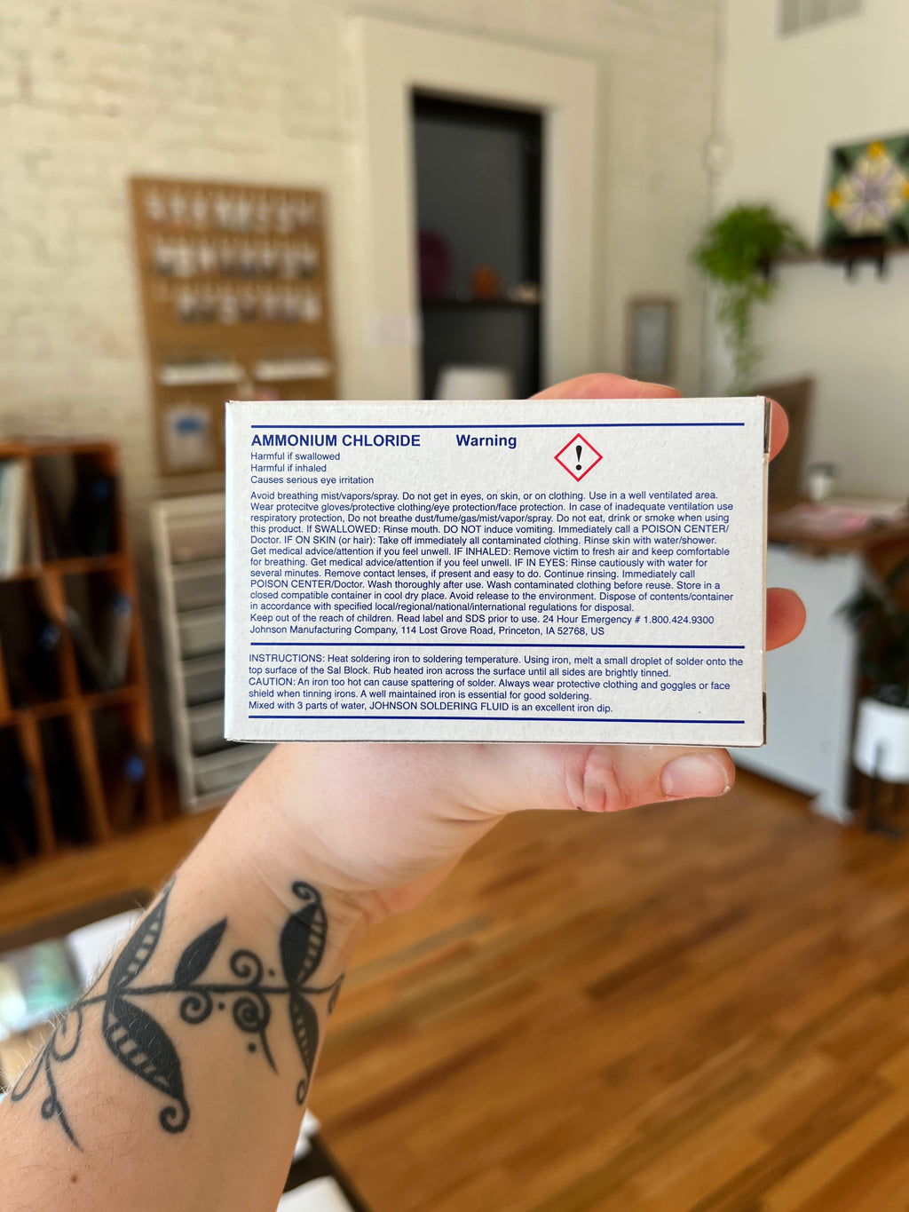 Hand holding a warning label for ammonium chloride in an indoor setting.