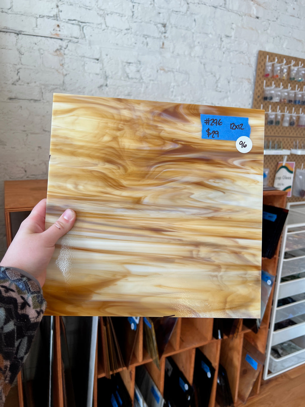 Hand holding a sheet of wood-patterned glass against a brick wall.