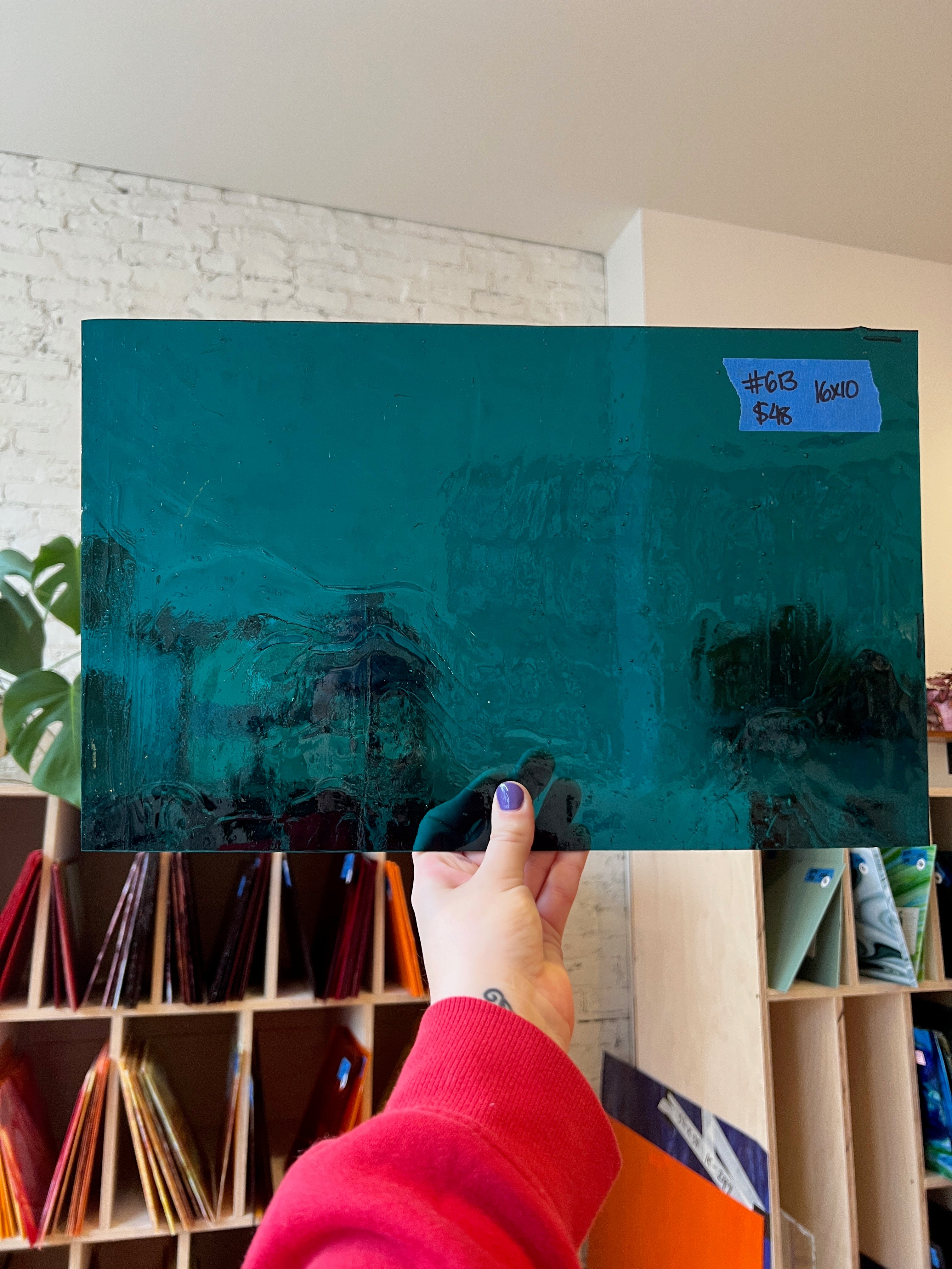 Person holding a large teal glass sheet with a blurred background