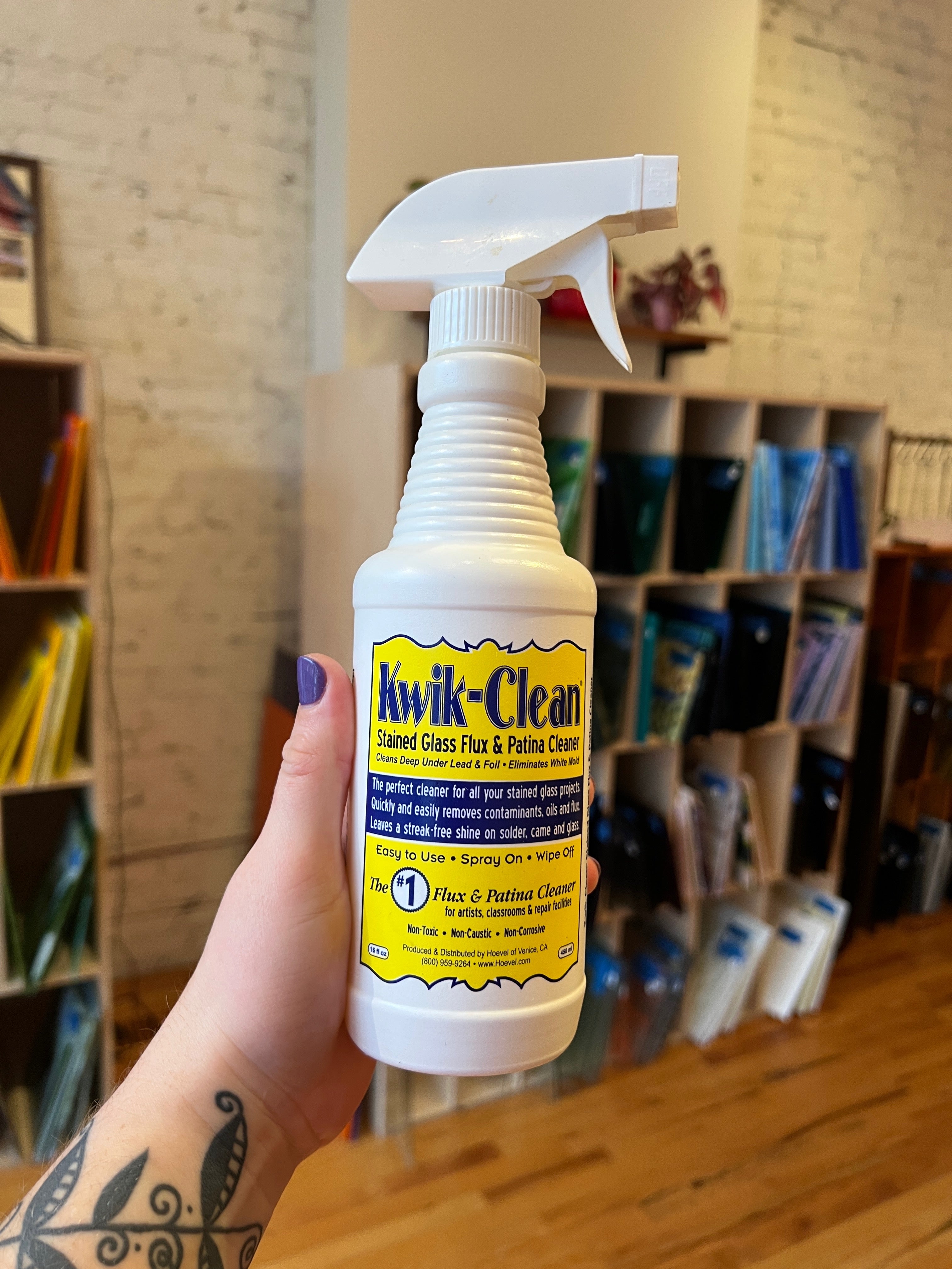 Hand holding a bottle of Kwik-Clean cleaner in a room with shelves and books.