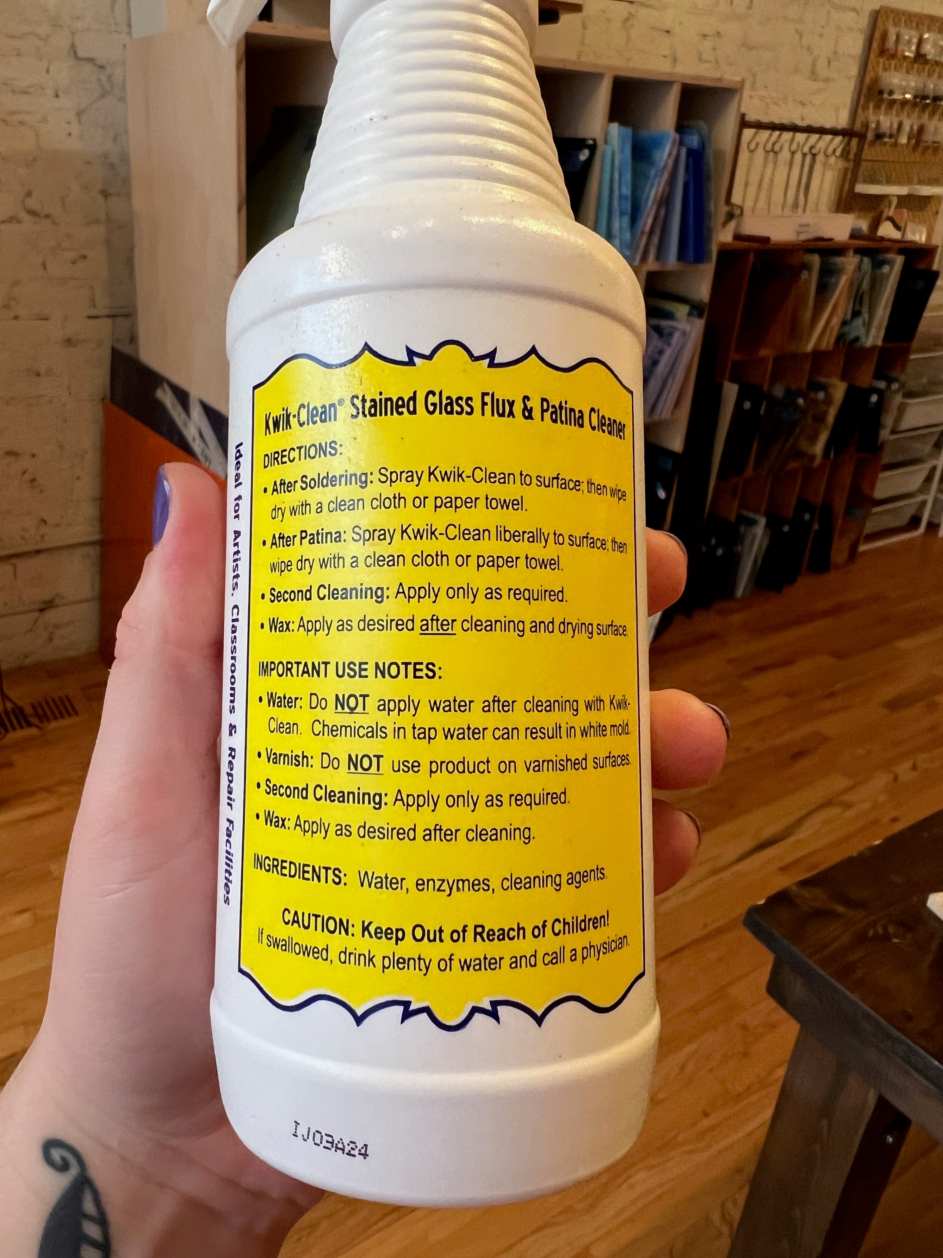 Hand holding a bottle of Kwik Clean Stained Glass Flux & Polishing Cleaner with a yellow label.