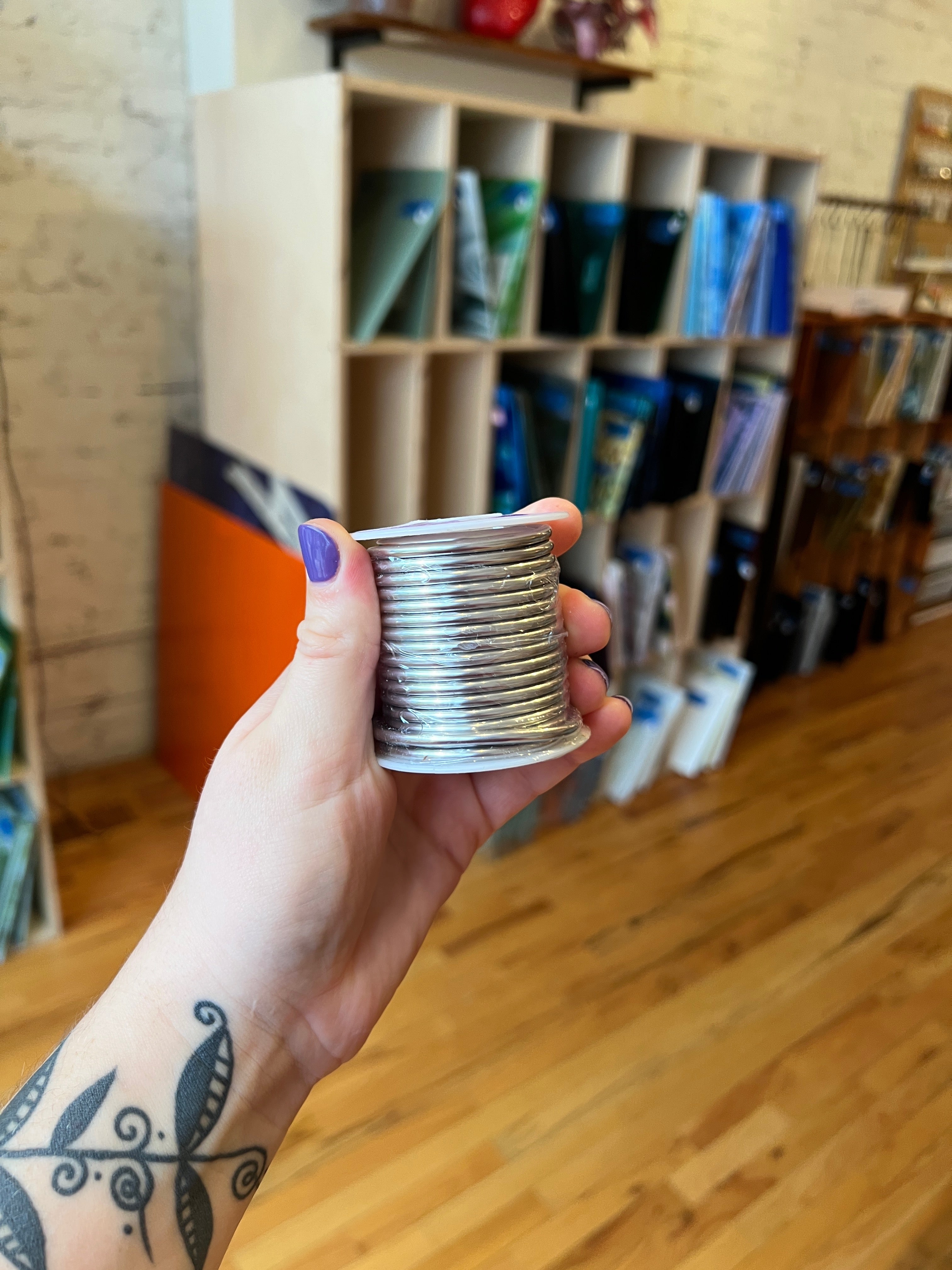 Hand holding a roll of solder with a bookshelf in the background