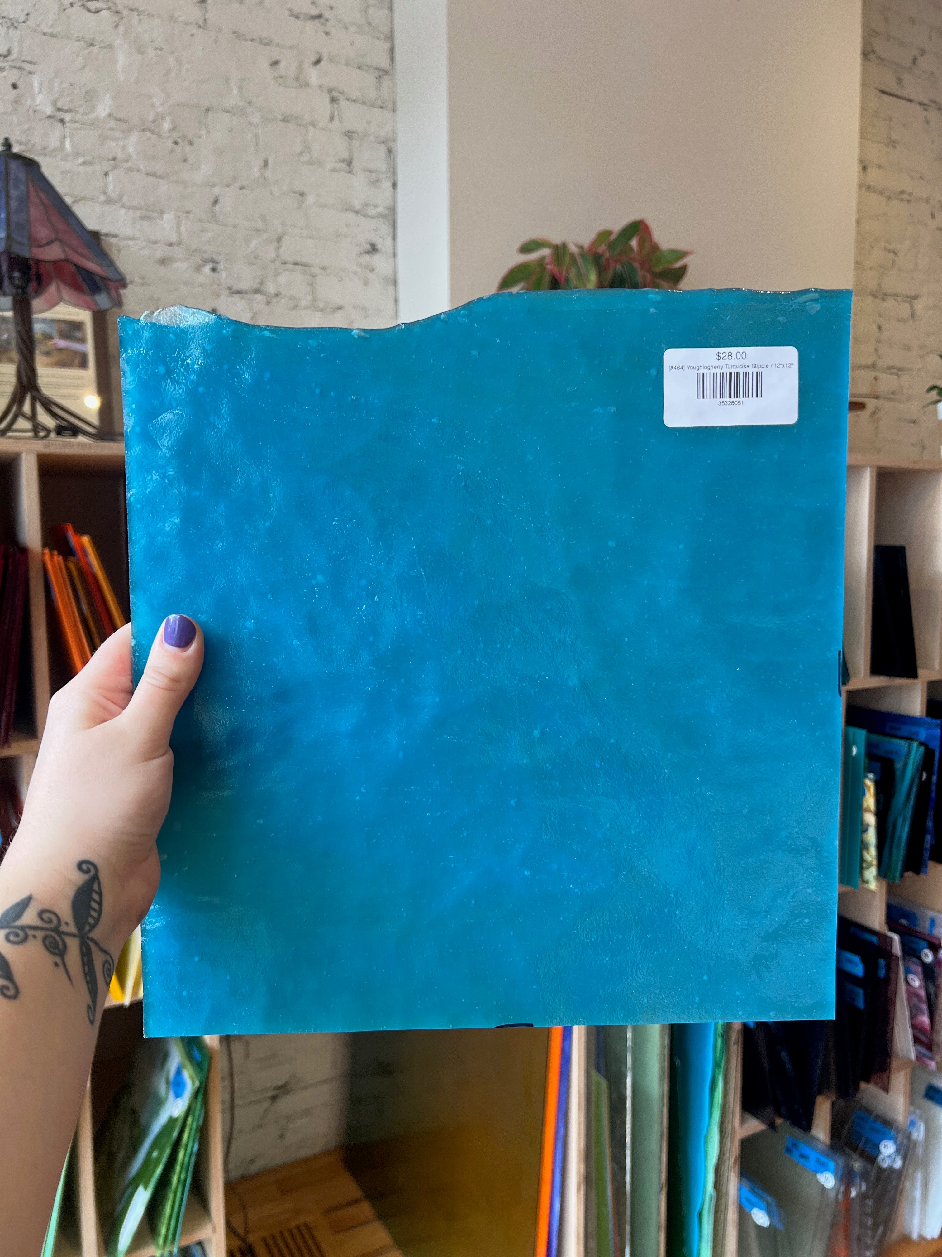 Hand holding a blue glass sheet against a shelf background