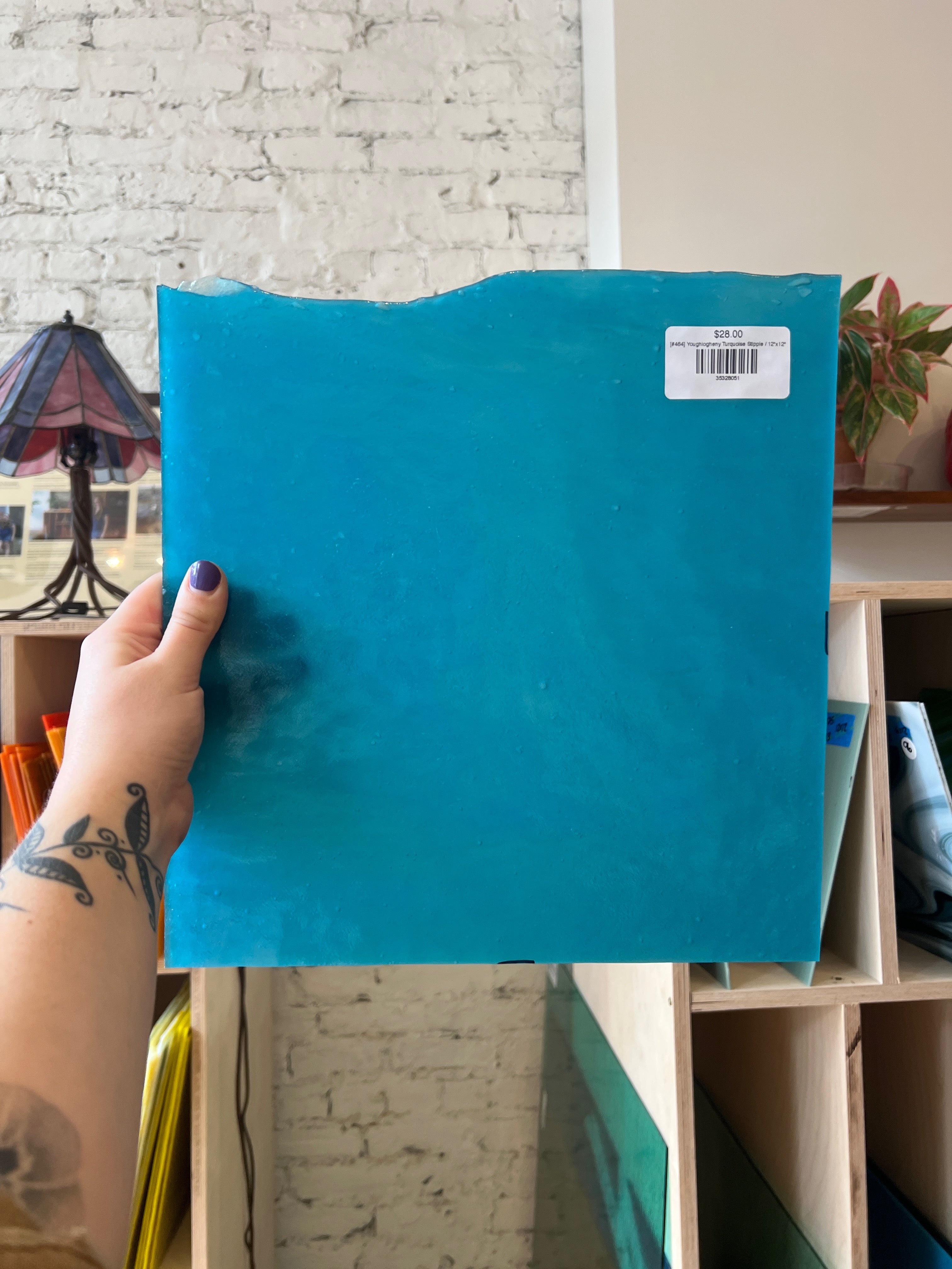 Person holding a blue glass sheet with a brick wall background