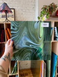 Person holding a piece of green marbled glass with a shelf in the background