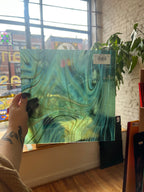 Person holding a piece of green marbled glass sheet with a store label in a room with large windows.