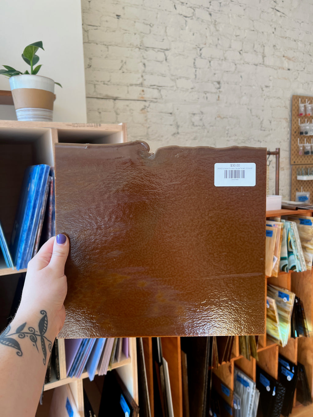 Person holding a brown sheet of glass with a brick wall background