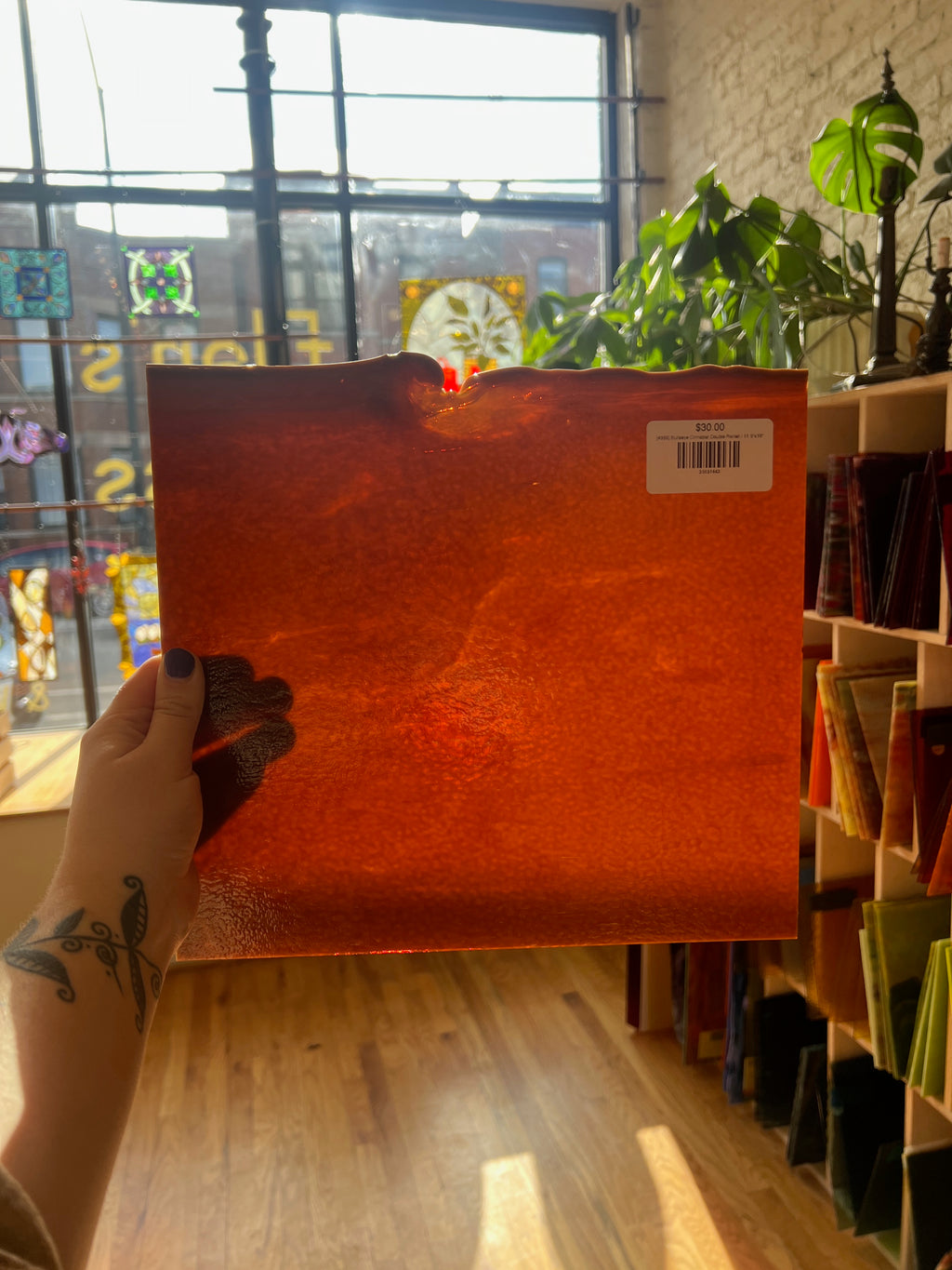 Person holding an orange sheet of glass in a store with plants and stained glass windows in the background.