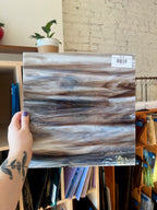 Person holding a wood-patterned sheet of glass with a blurred indoor background