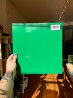 Person holding a green sheet of glass with a barcode in a room with wooden flooring and furniture.
