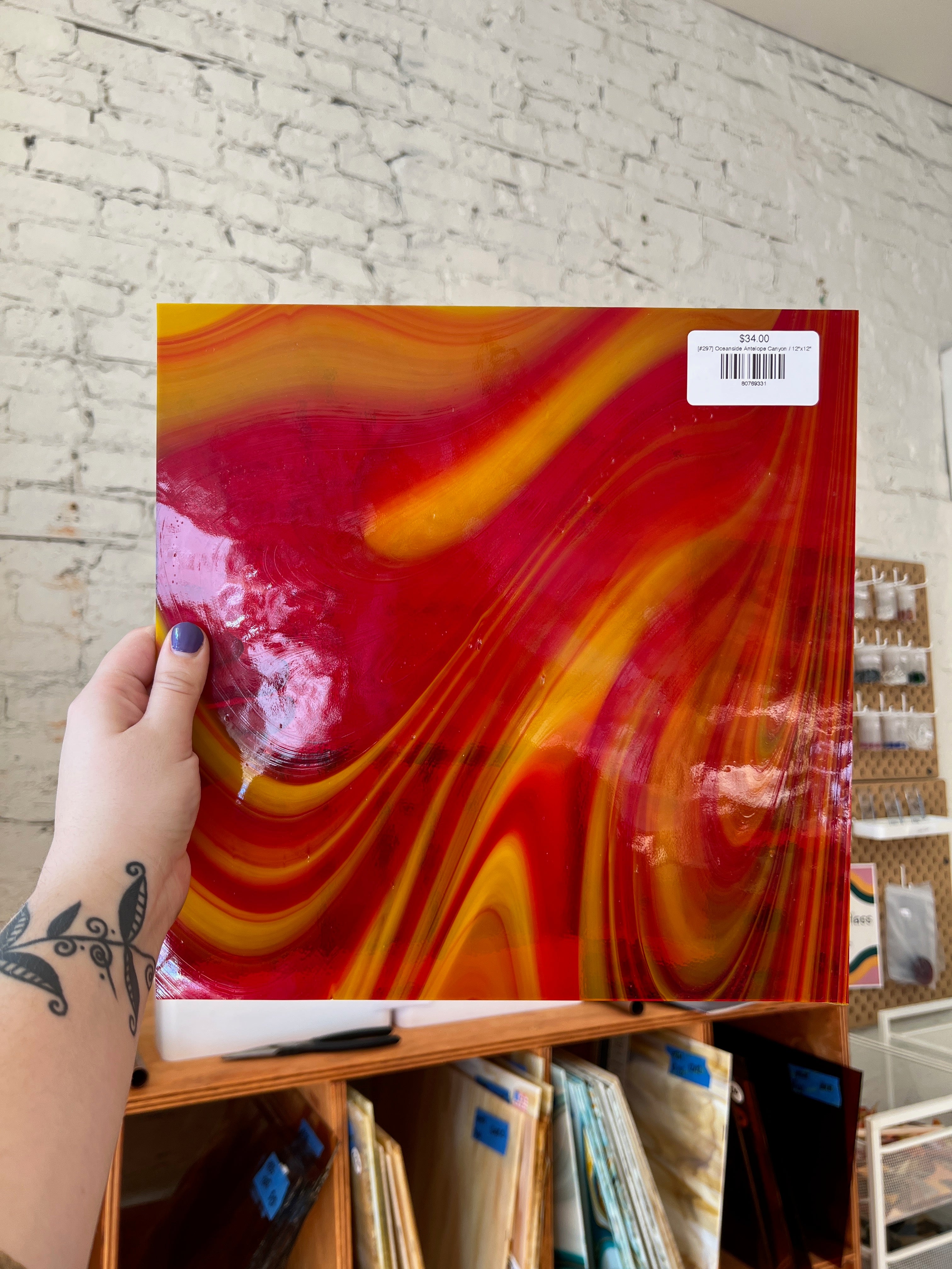 Person holding a colorful glass sheet with a brick wall background