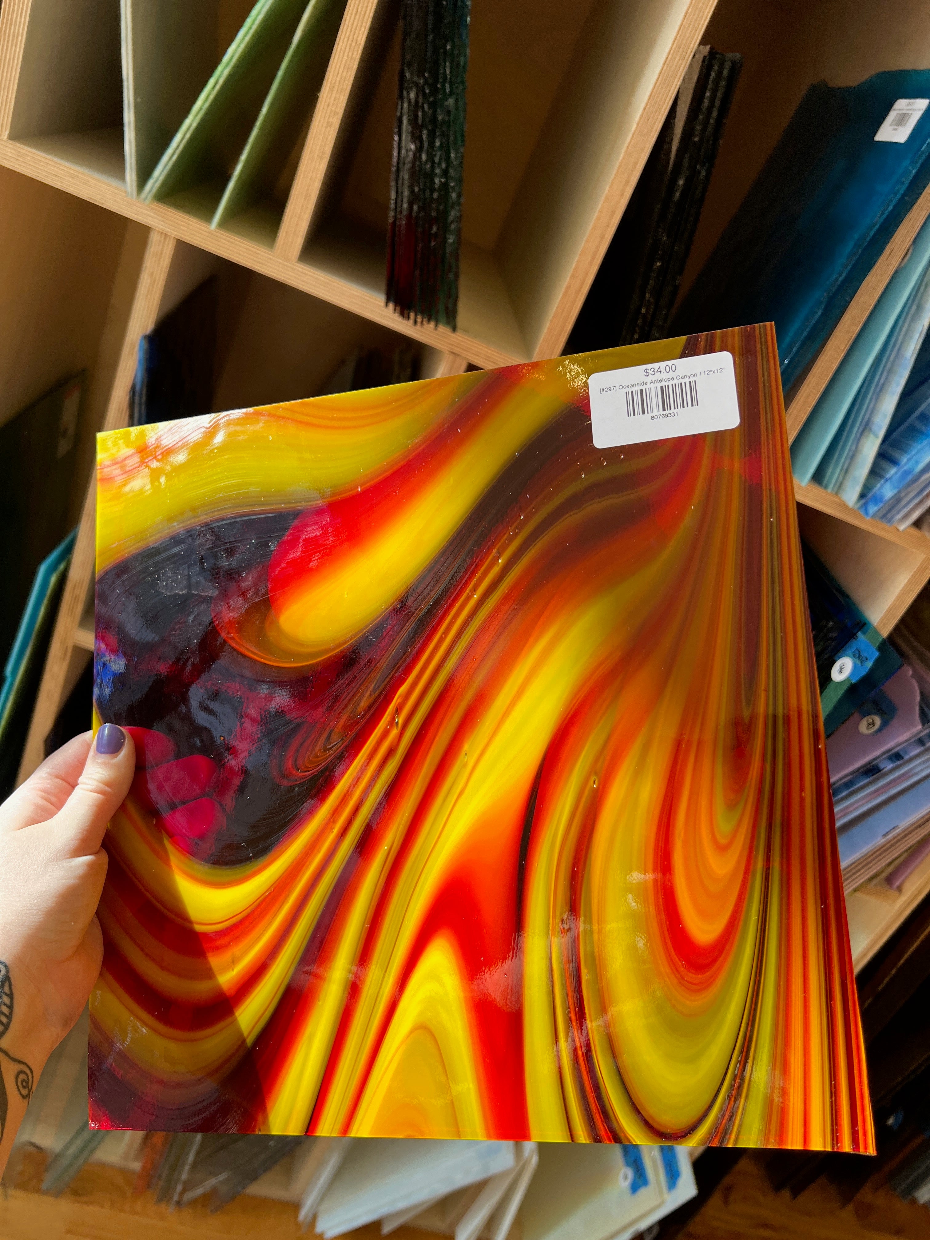 Colorful abstract glass sheet held by a hand with a blurred shelf background