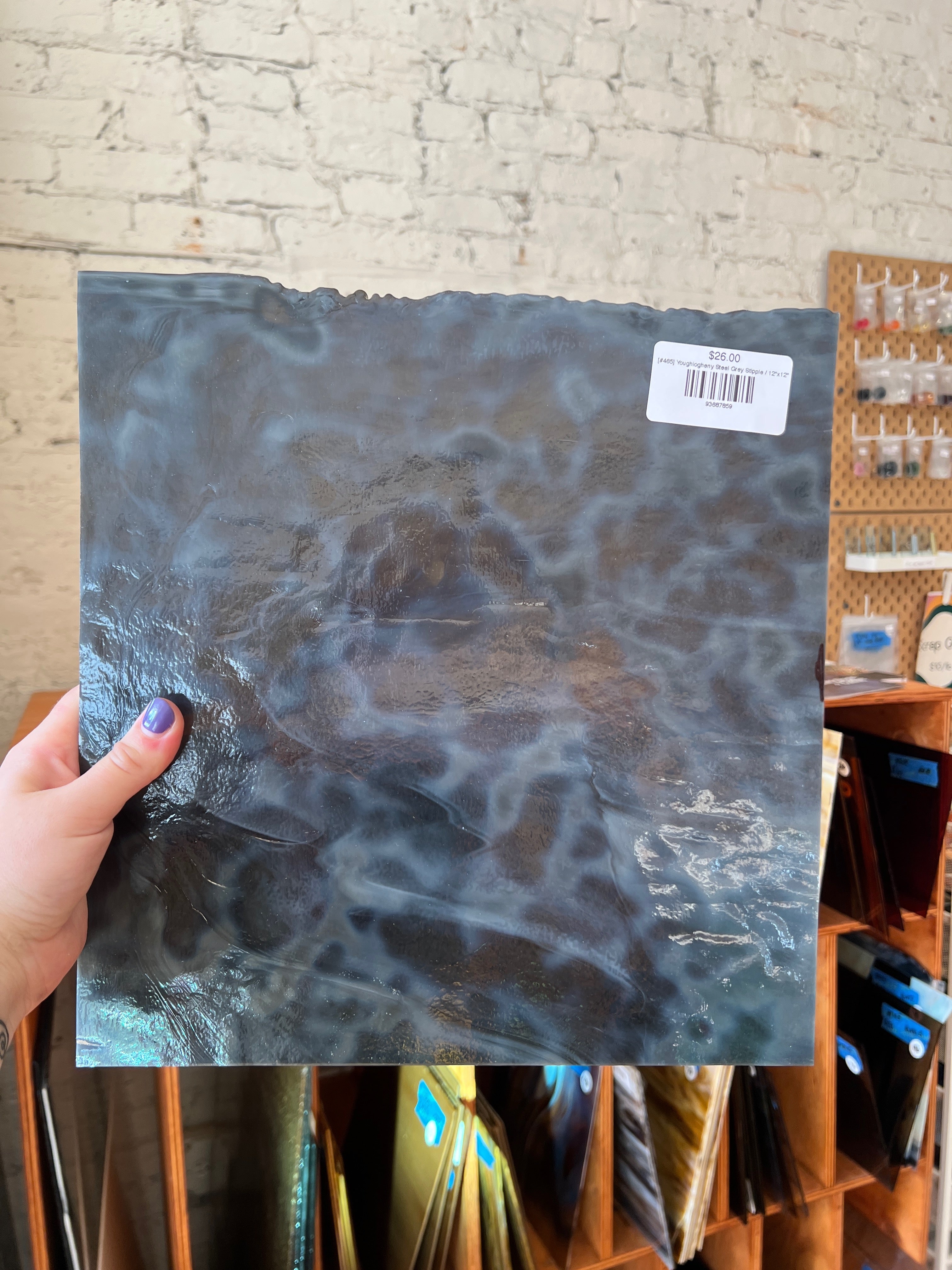 Person holding a textured blue sheet of glass in front of a brick wall.