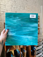 Turquoise marbled glass held by a hand with a tattoo, against a brick wall.