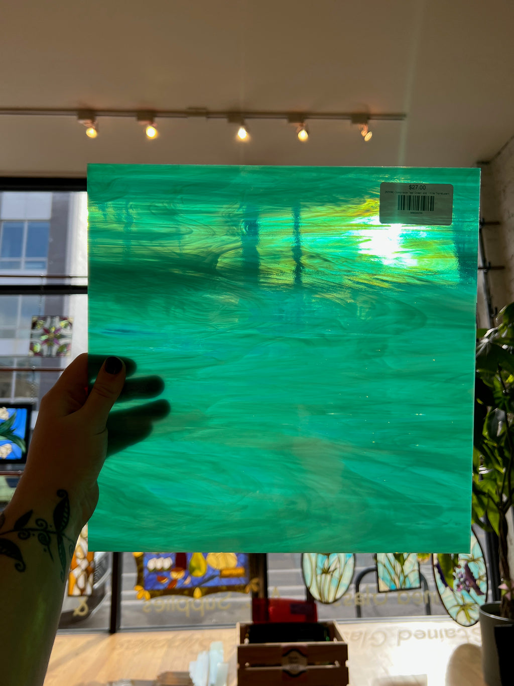 Turquoise sheet glass held by a hand in front of a store window with various items displayed.