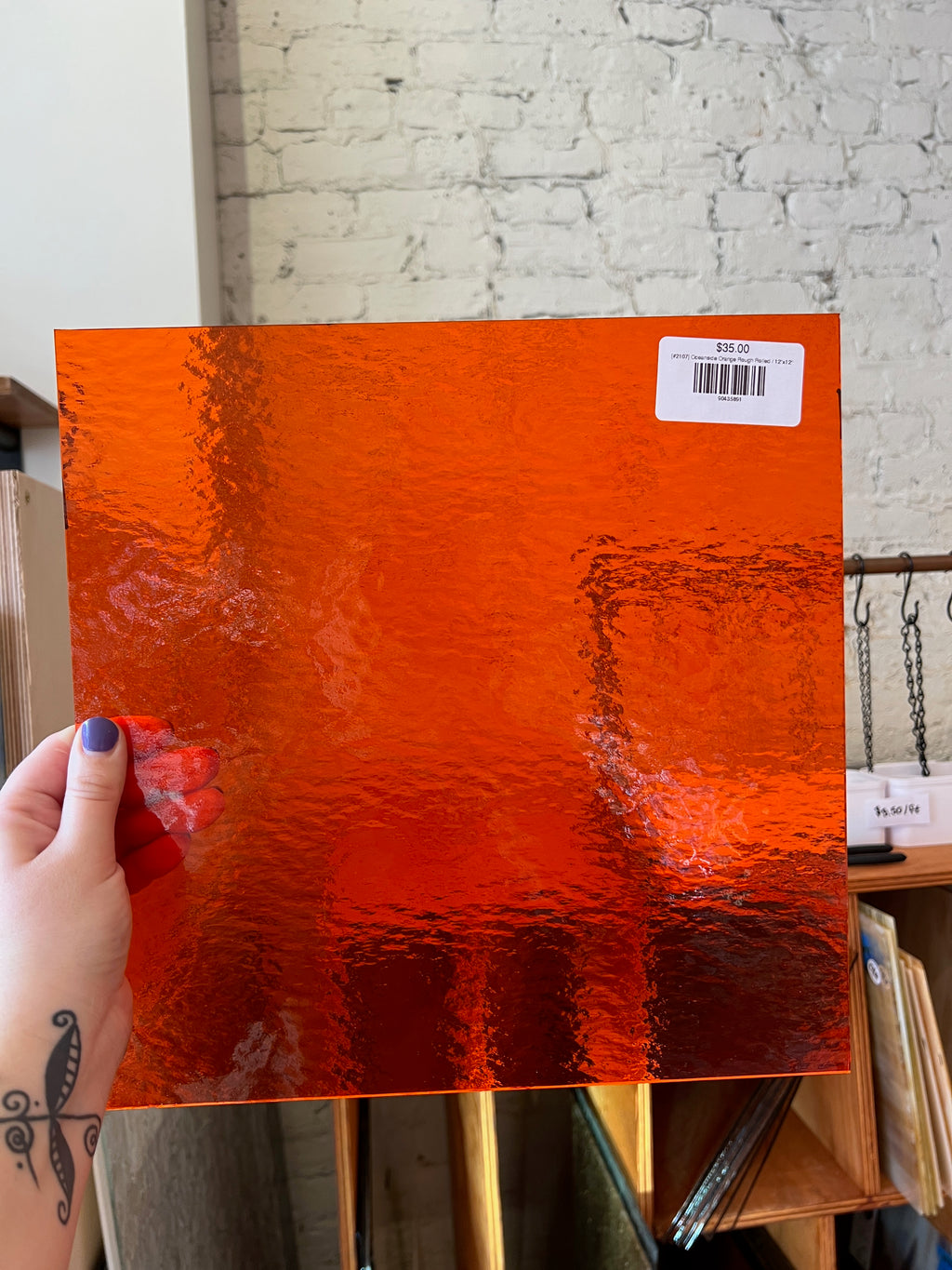 Person holding a textured orange sheet of glass with a barcode label against a brick wall.