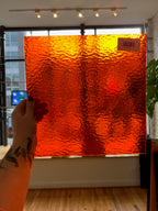 Hand holding a large orange glass panel indoors with a blurred background