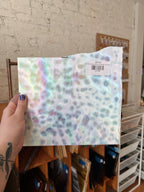 Hand holding a piece of iridescent sheet glass with a blurred indoor background