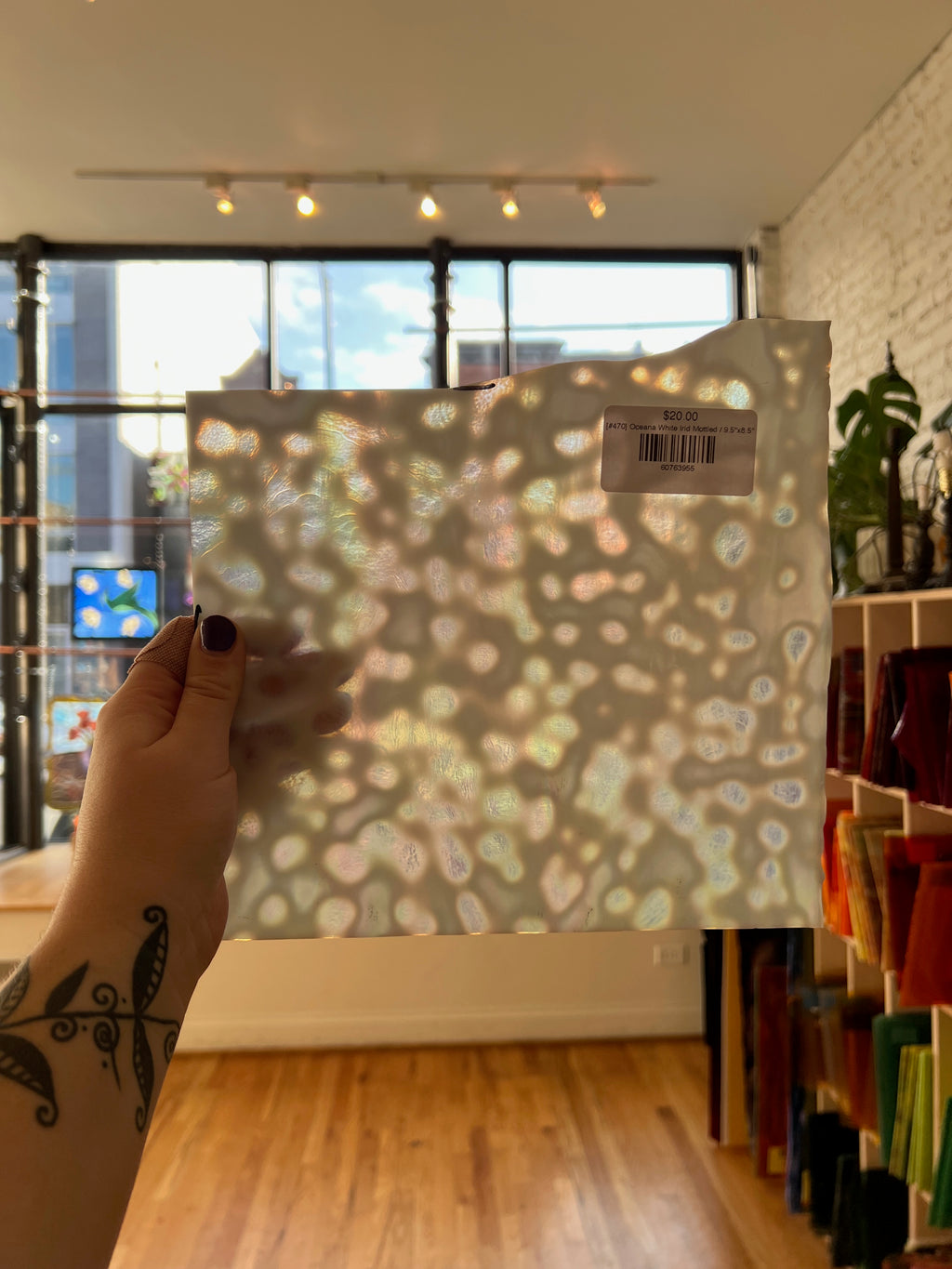Hand holding a patterned sheet of glass in front of a window with a cityscape view.