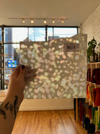 Hand holding a patterned sheet of glass in front of a window with a cityscape view.