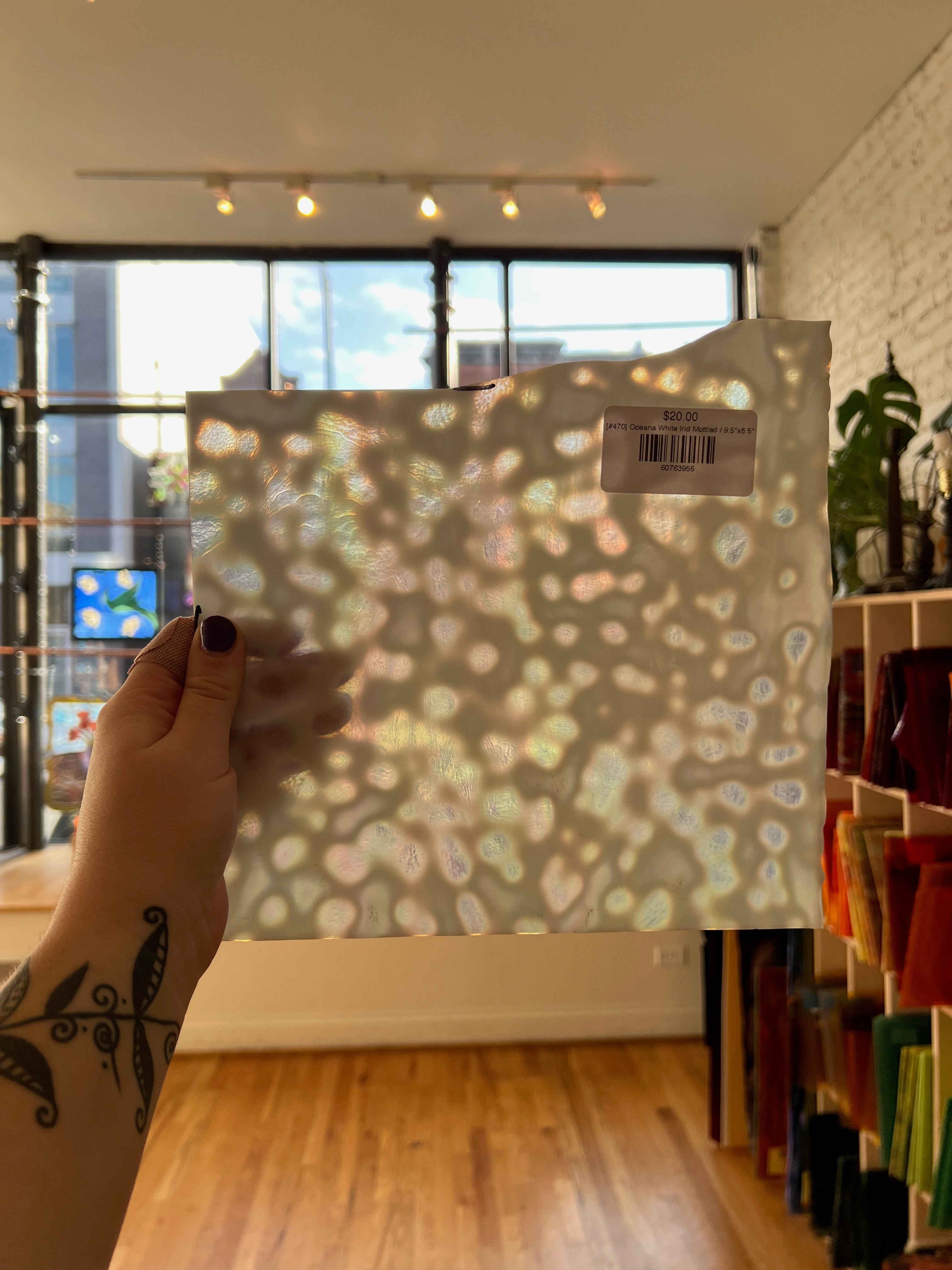 Hand holding a patterned sheet of glass in front of a window with a cityscape view.