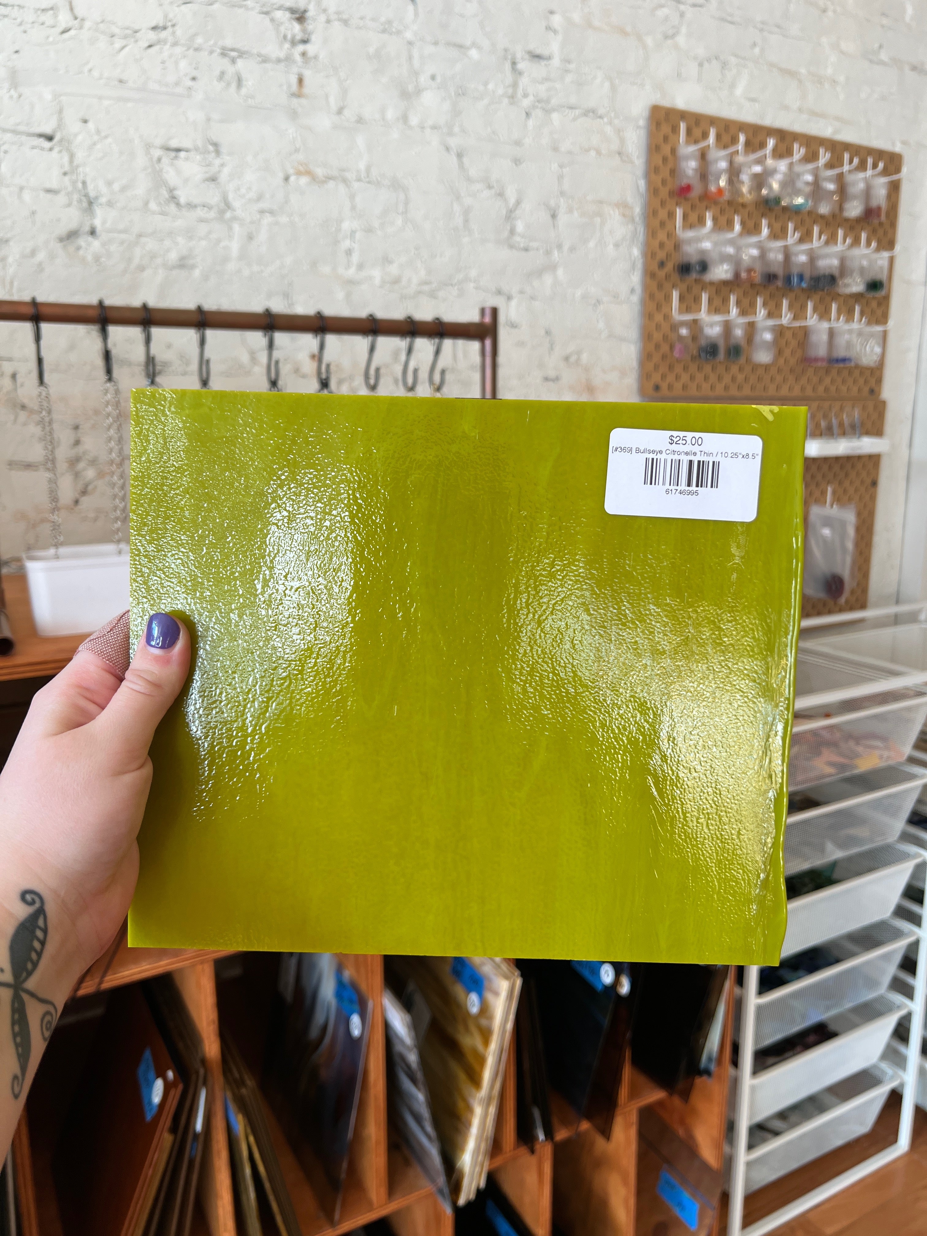 Hand holding a green textured sheet of glass with a label against a background of shelves and storage units.