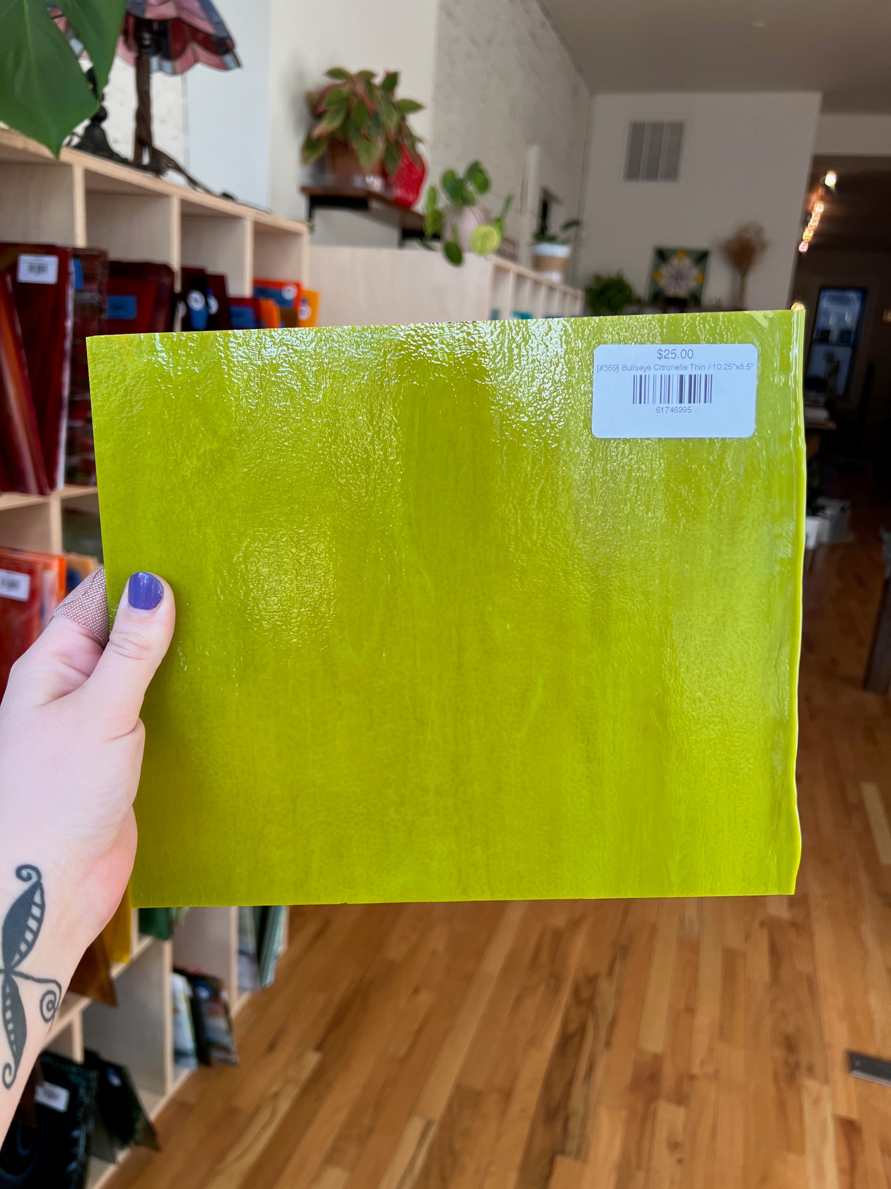 Person holding a bright green sheet of glass with a barcode label in a store setting.
