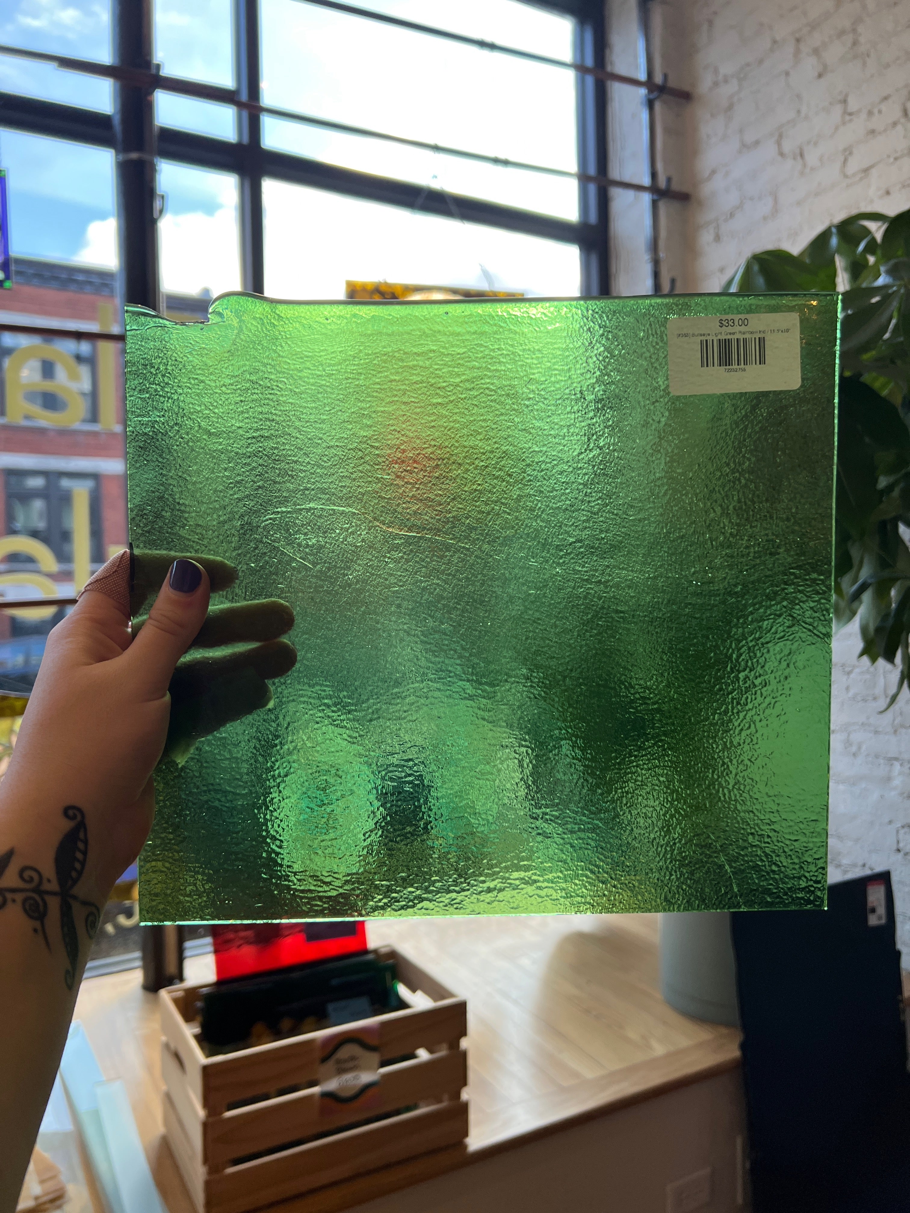 Green textured glass panel held by a hand with a tattoo, indoors.