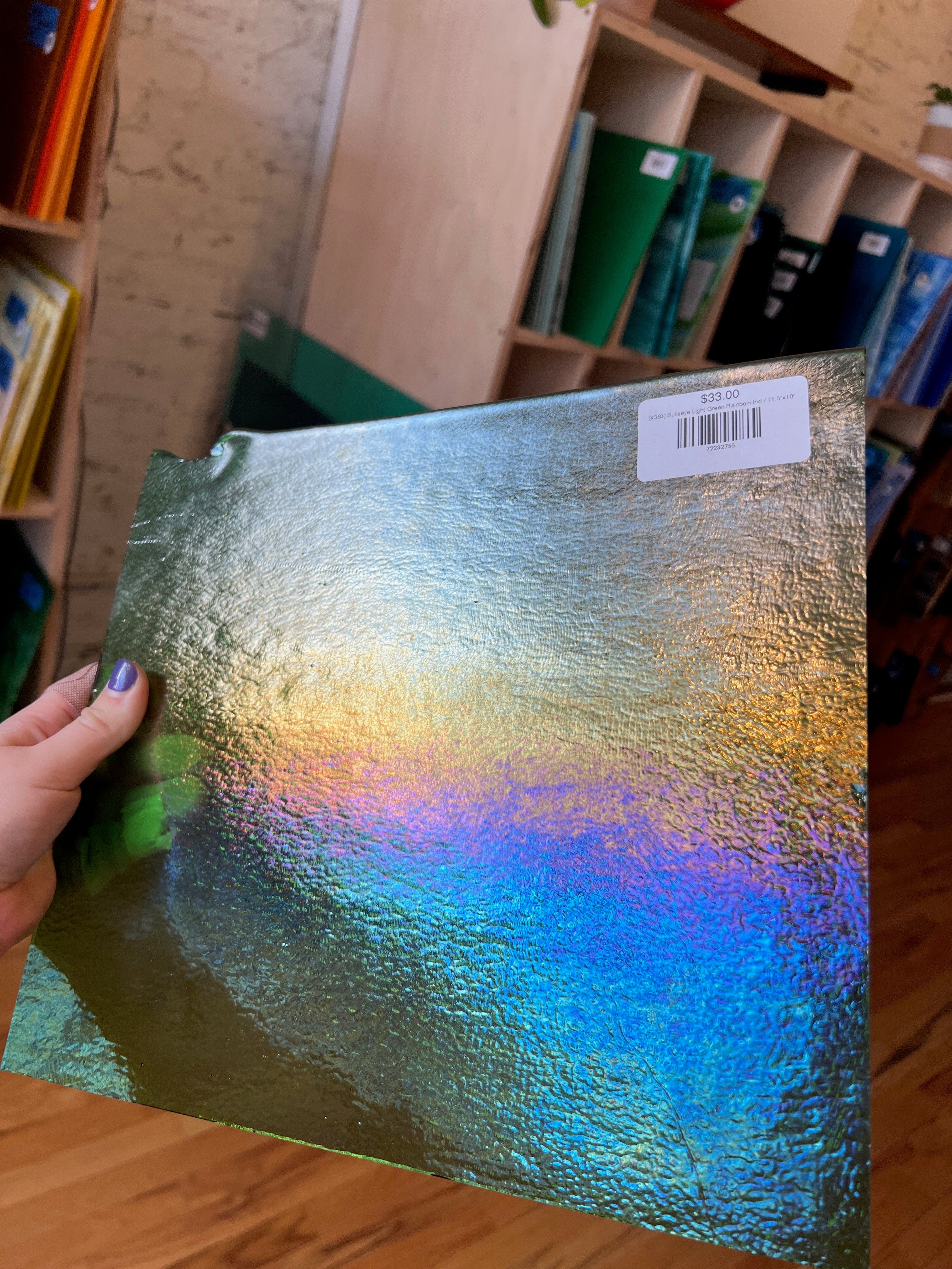 Iridescent glass sheet held by a hand in a room with shelves in the background