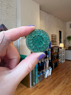 Hand holding a green decorative glass gem with a blurred indoor background