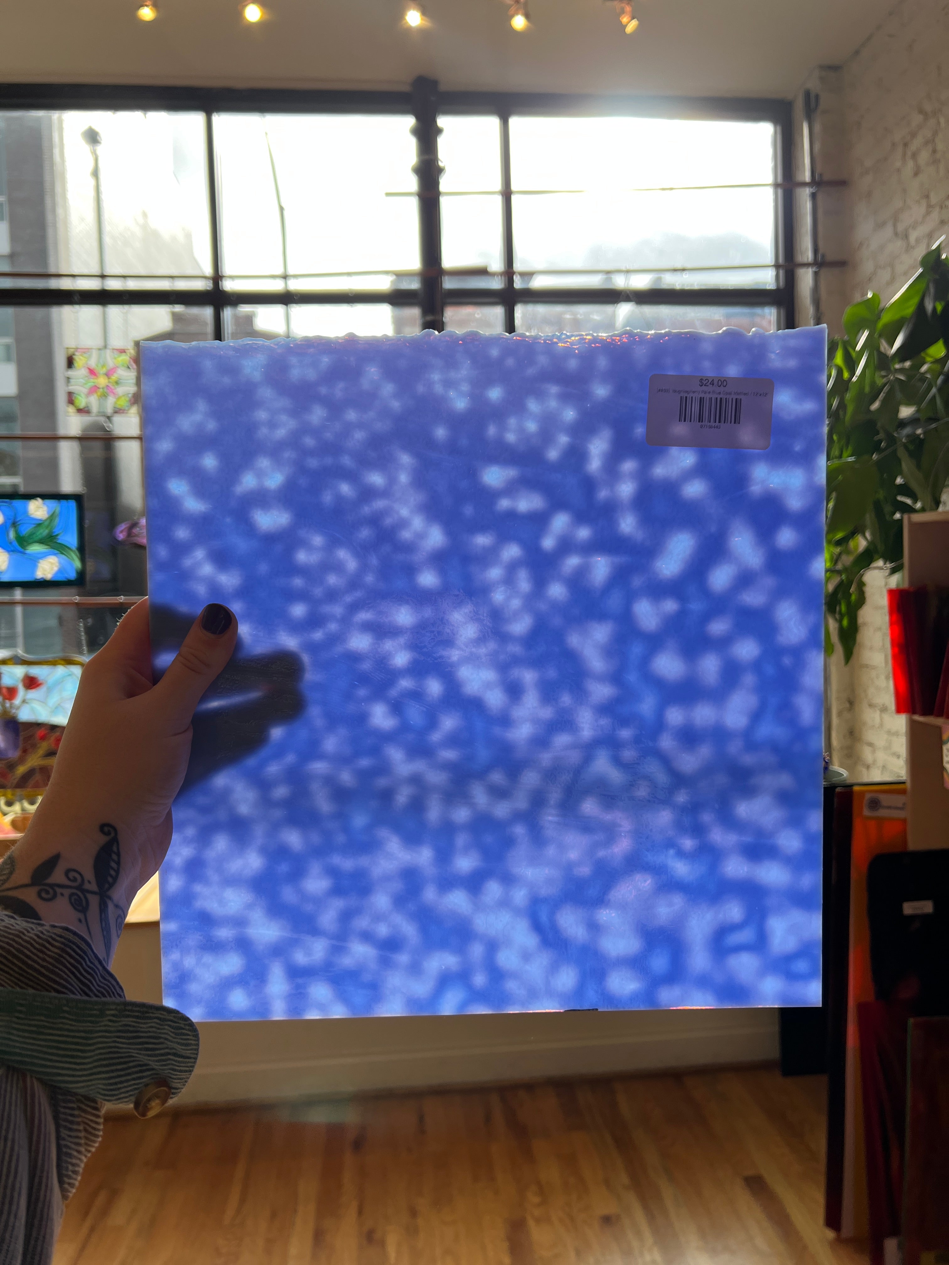 Blue textured glass sheet held by a person in a room with a window and plant