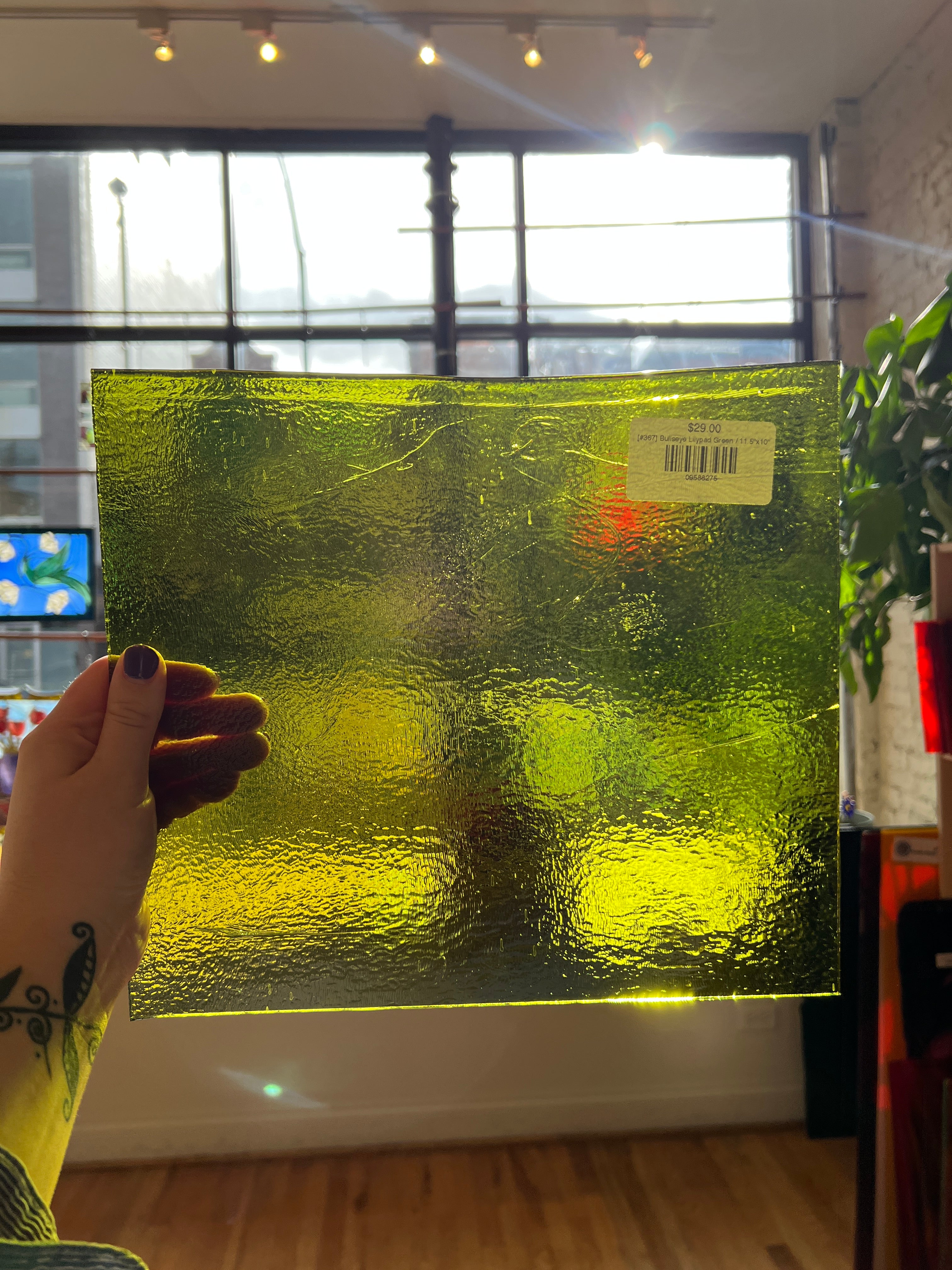 Green textured glass panel held by a hand with a tattoo, indoors.