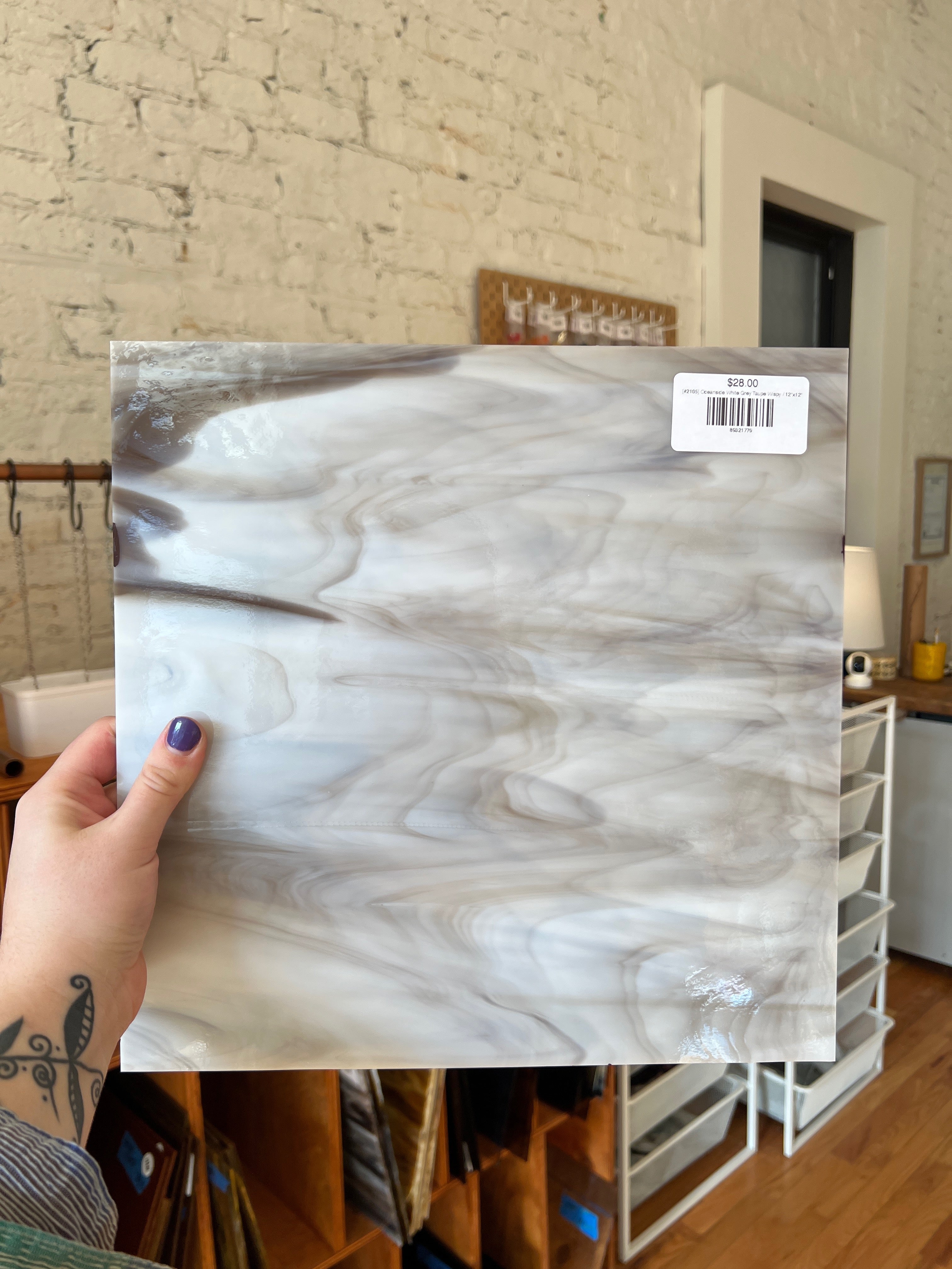 Person holding a sheet of grey marble-patterned glass against a brick wall.