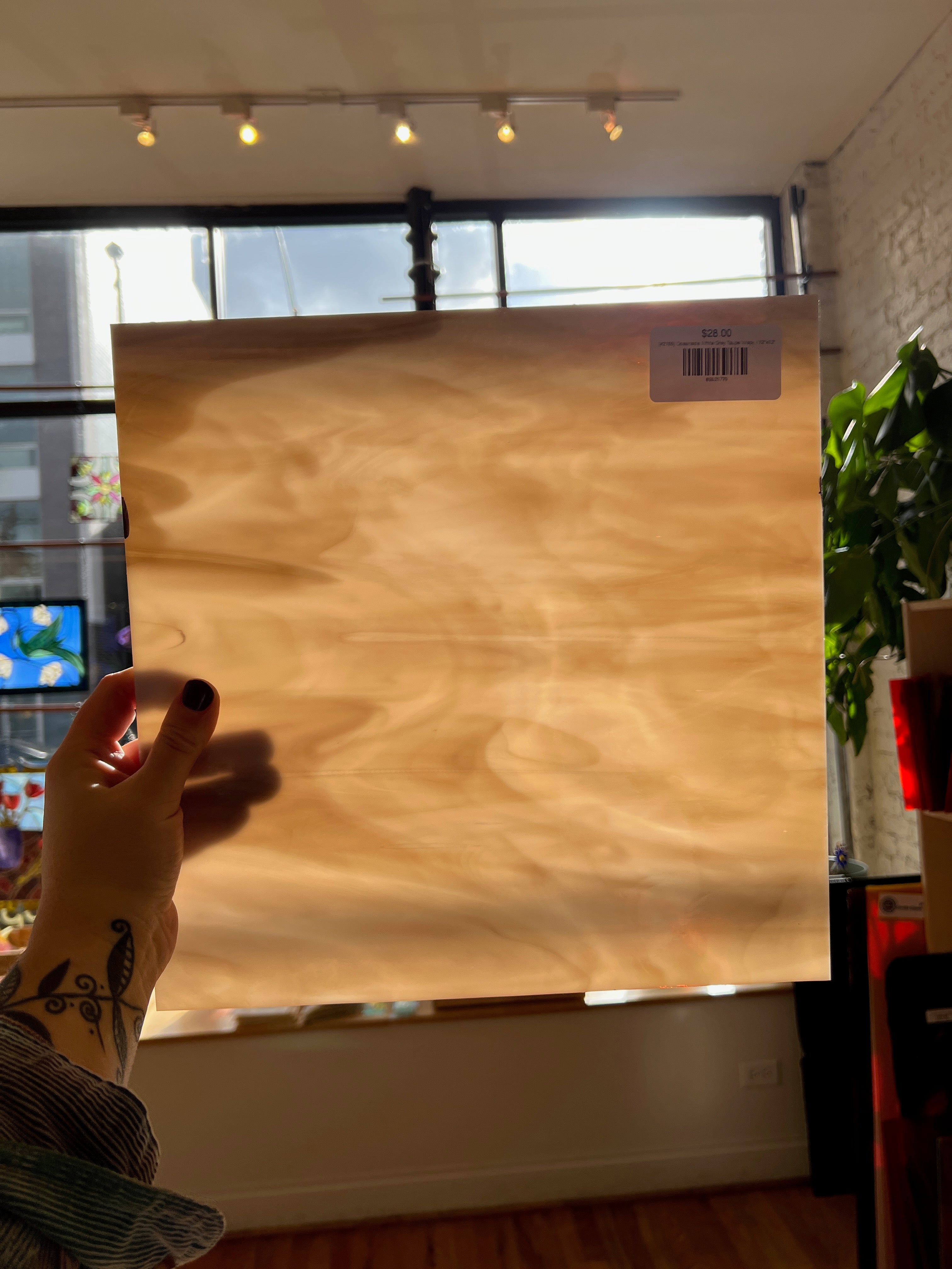 Person holding a large brown glass panel with a visible brand label in an indoor setting.