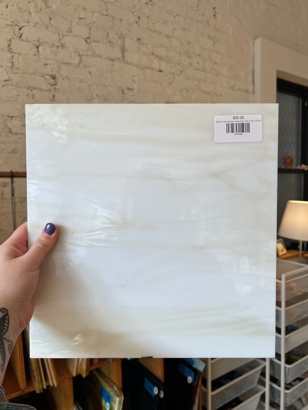 Person holding a white glass sheet with a visible barcode against a brick wall.
