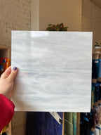 White marble-patterned glass held by a hand in front of a shelf.