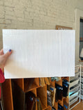 Person holding a white sheet of glass against a brick wall.