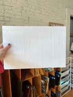 Person holding a white sheet of glass against a brick wall.