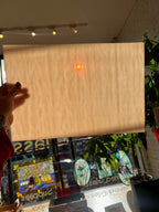 Person holding a light brown piece of glass in front of a store window with stained glass.