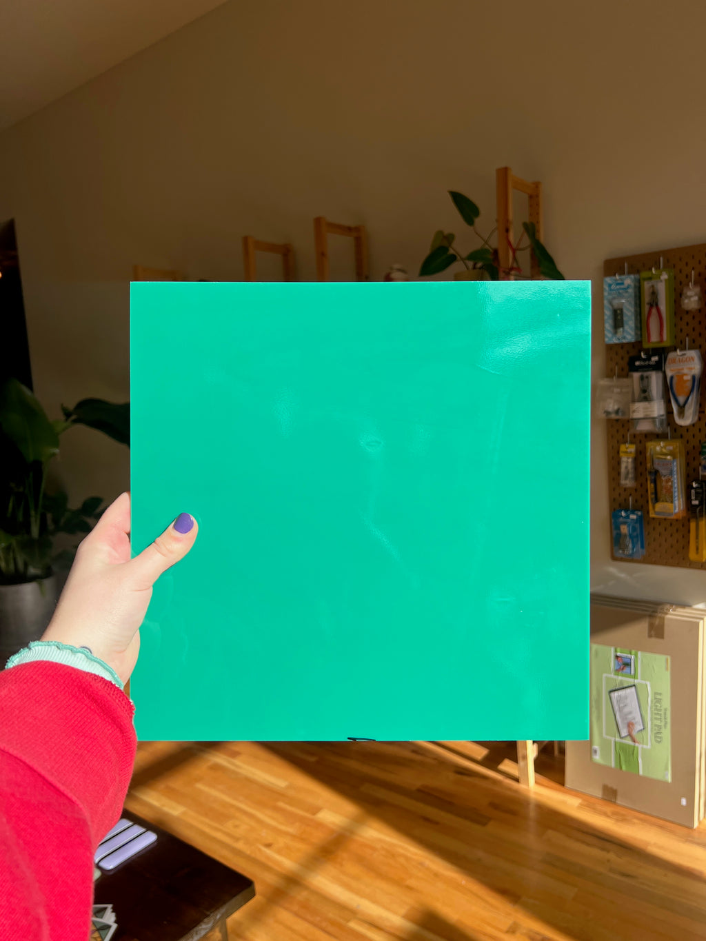 Hand holding a teal square of glass in front of a room with a table and plants.