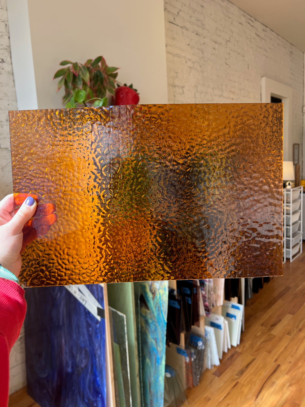 Person holding a textured brown piece of stained glass in a room with plants and furniture.