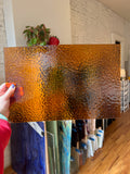 Person holding a textured brown piece of stained glass in a room with plants and furniture.