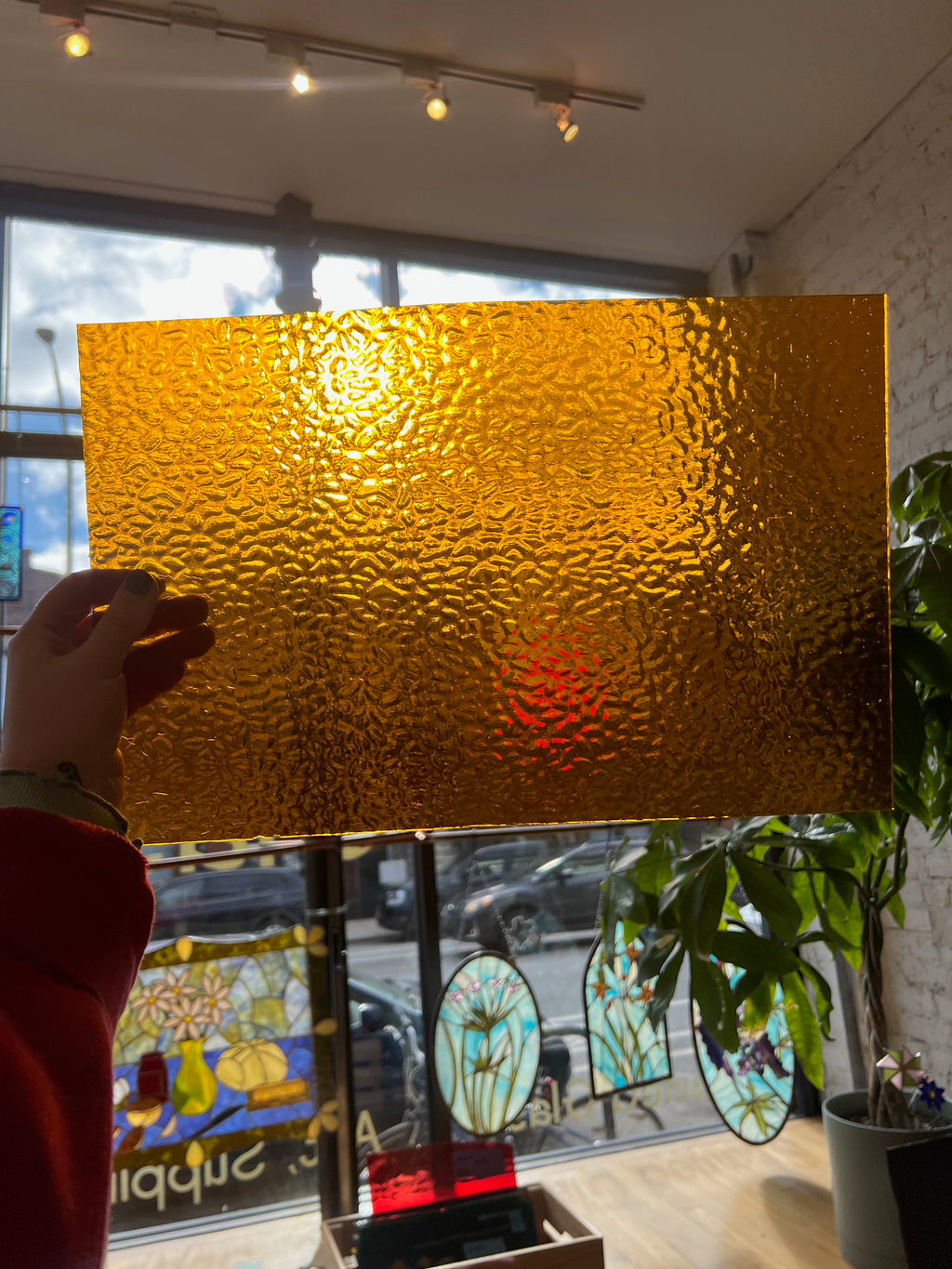 Gold textured glass panel held by a person in front of a store window with stained glass.