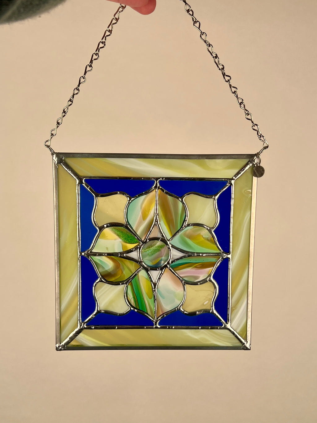 Stained glass panel with floral design on a blue background, held by a chain against a beige background.