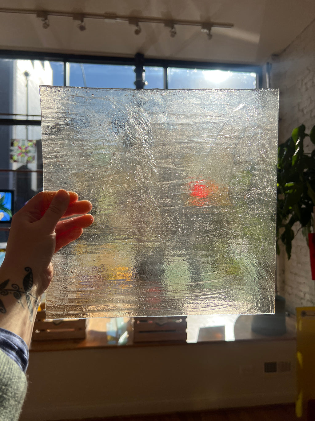 Hand holding a transparent sheet of textured stained glass in front of a window