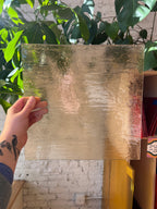 Hand holding a piece of transparent gold stained glass with a blurred background