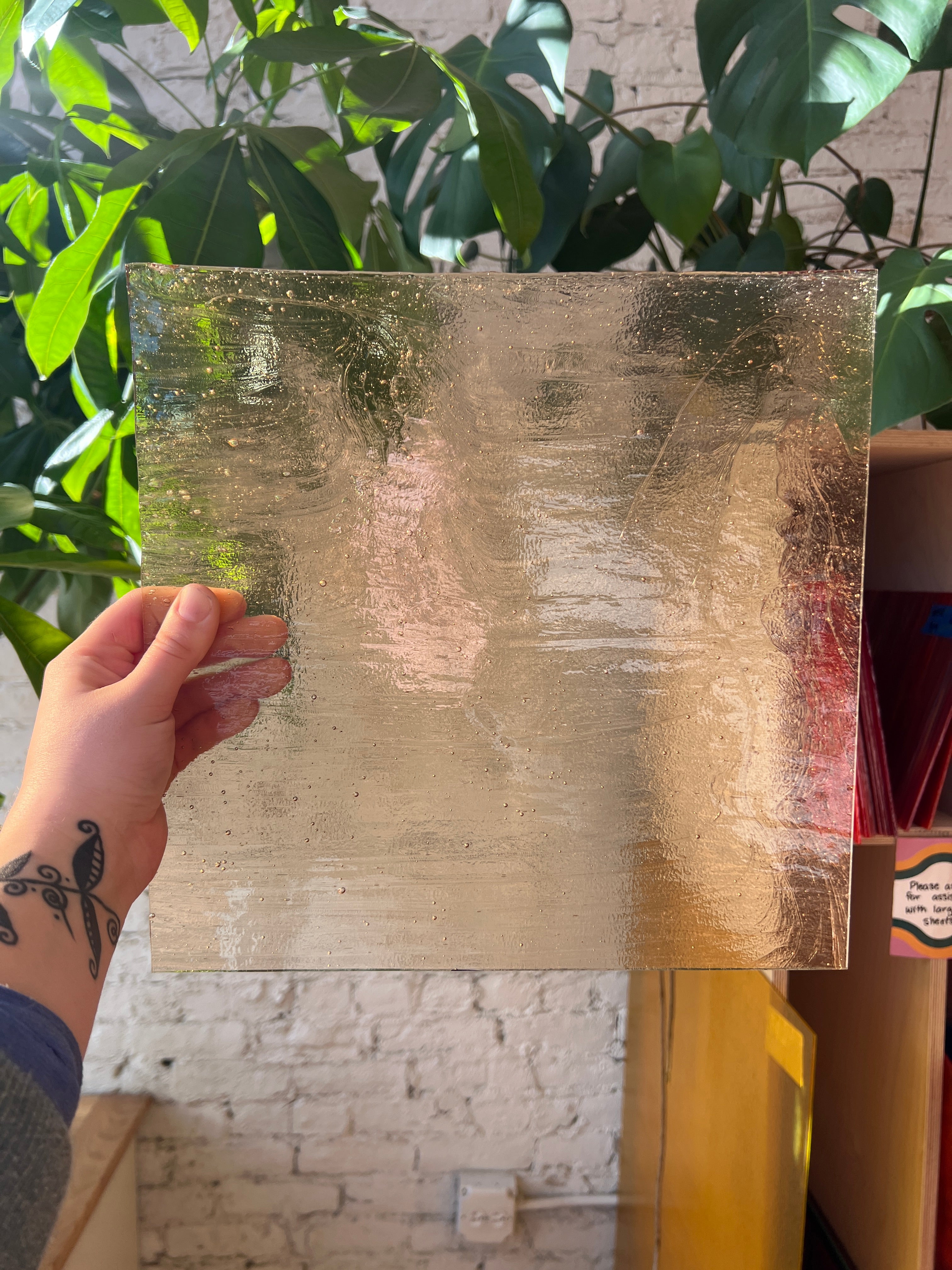 Hand holding a piece of transparent gold stained glass with a blurred background
