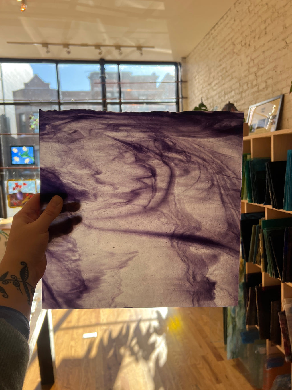 Person holding a piece of purple swirled stained glass in a store setting