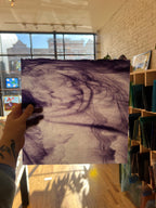 Person holding a piece of purple swirled stained glass in a store setting