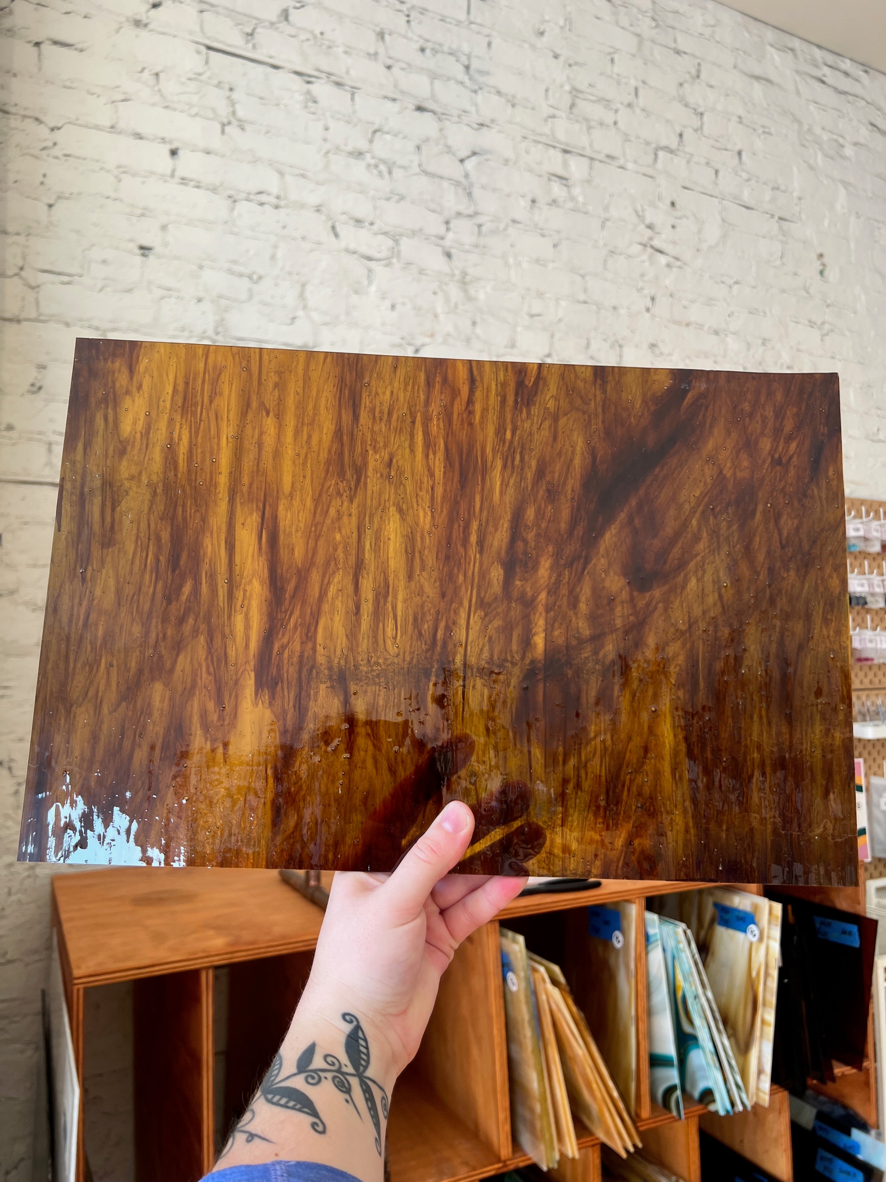 Person holding a brown swirled piece of glass against a brick wall.